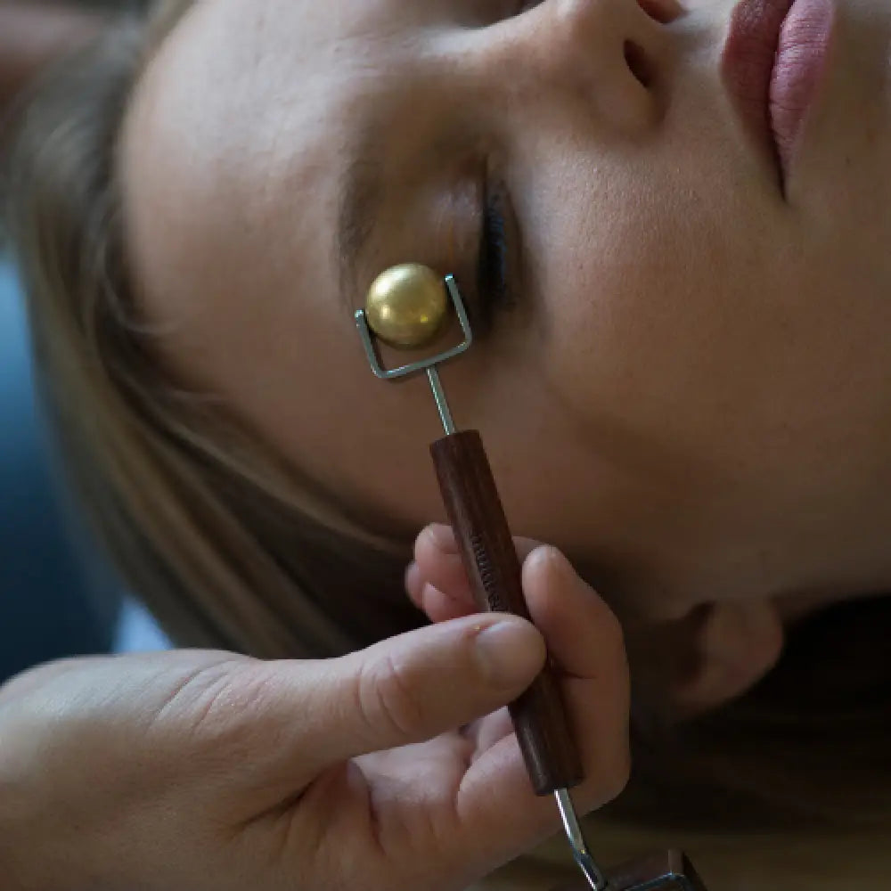Gold and brown wooden concave facial roller with brass ball ends