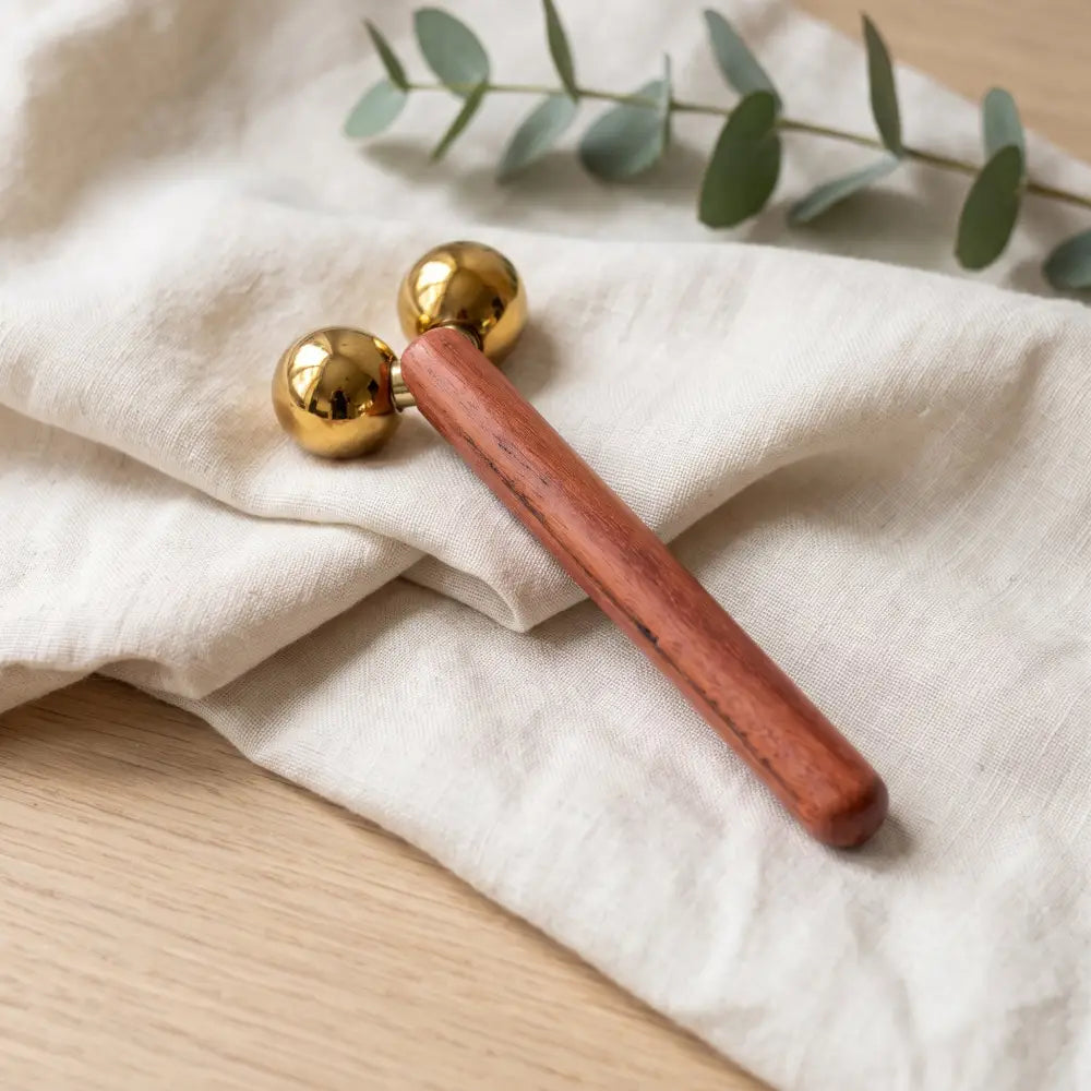 A sleek wooden face roller nº302 double sphere with two polished gold-toned spherical ends for facial massage